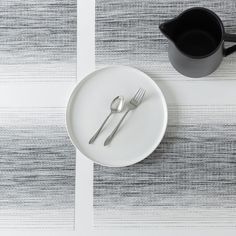 a white plate topped with a fork and knife next to a black cup on top of a table