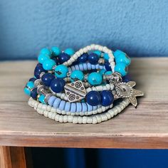 The Seven Seas bracelet is an island inspired piece that features beautiful shades of blue ( turquoise, royal blue and periwinkle) combined with silver beads and enchanting charms. Wear it with your resort outfits to elevate your look! Bracelet Stack Summer, Seed Bracelets, Blue And White Bracelet, Resort Outfits, Resort Jewelry, Blue Periwinkle, White Bracelet, Seven Seas, Resort Outfit