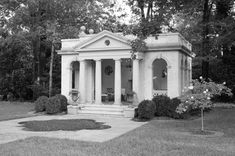 black and white photograph of an old house with columns in the front yard, surrounded by trees