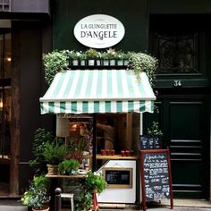 an outside view of a store with plants on the front and green awnings