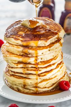 a stack of pancakes with syrup being drizzled over them and topped with raspberries