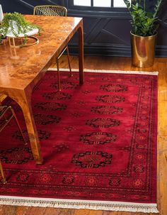 a red rug is on the floor next to a wooden table and potted plants