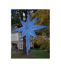 a large blue christmas star hanging from the side of a tree in front of a house