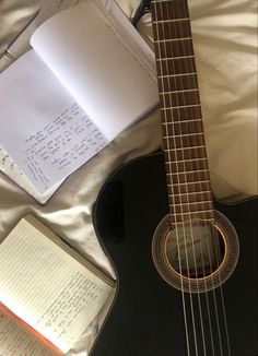 an acoustic guitar and notebooks on a bed