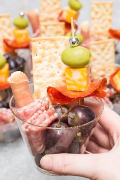 a hand holding a glass filled with fruit and crackers