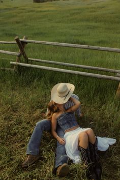 a man and woman laying on the ground in front of a wooden fence with horses behind them