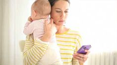 a woman holding a baby and looking at her cell phone while she holds it up to her ear