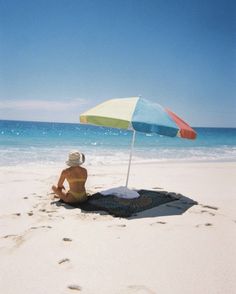 a woman sitting under an umbrella on the beach