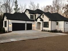 a white house with black roof and two garages