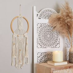 a white wall hanging next to a vase with a candle on it and a decorative dream catcher