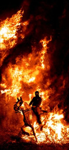 a man riding a horse in front of a huge fire filled sky with flames behind him