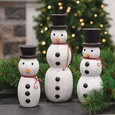 three snowmen standing next to each other on top of a table near a christmas tree