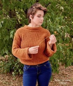 a woman in an orange sweater is holding a flower and looking down at her hand