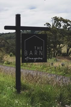 a black sign sitting on the side of a road next to a lush green field