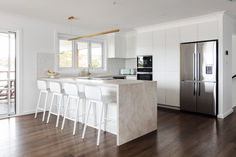 a kitchen with white cabinets and marble counter tops next to a stainless steel refrigerator freezer