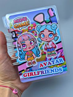 a hand holding a mini game book with two girls on it