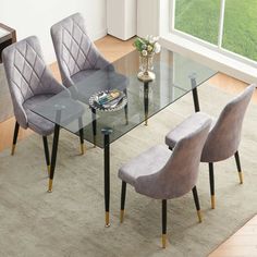 a glass dining table with four chairs and a vase on the floor next to it