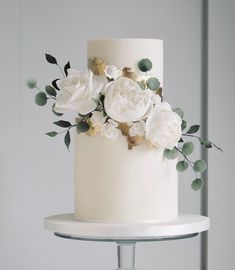 a three tiered white cake with flowers on top and greenery around the edges