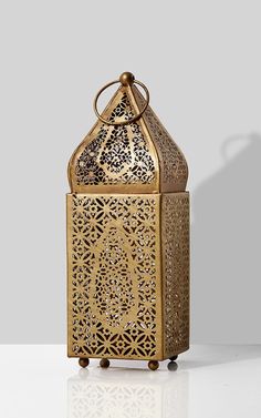 an intricately designed golden metal box on a white surface with a shadow from the side