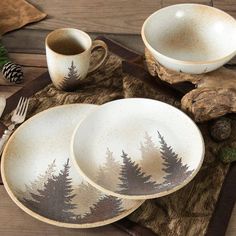 three white dishes with pine trees painted on them are sitting on a placemat next to two forks and spoons