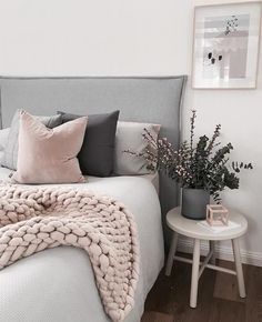 a white bed topped with lots of pillows next to a vase filled with pink flowers