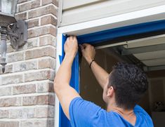 a man in blue shirt working on an open garage door with the light on and one hand up