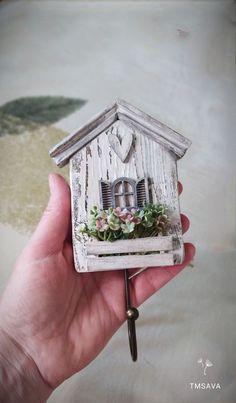 a hand holding a small white birdhouse with flowers on the window sill and door