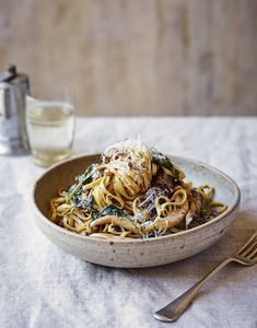 a white bowl filled with noodles and meat on top of a table next to a glass of water