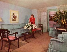 a woman standing in a living room next to a blue couch and table with flowers on it