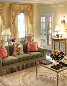 a living room filled with lots of furniture and flowers on the coffee table in front of a window