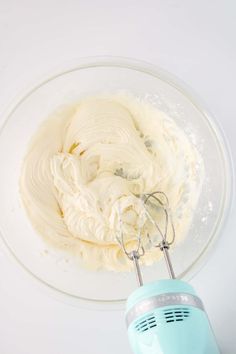 a mixing bowl filled with whipped cream on top of a white counter next to an electric hand mixer