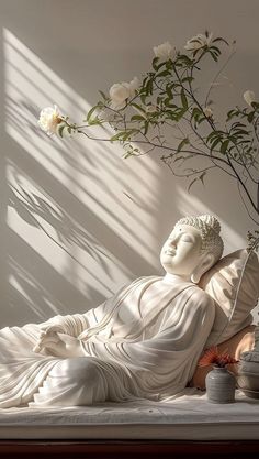 a white buddha statue sitting on top of a bed next to a vase filled with flowers