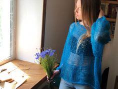 a woman standing in front of a window holding a bouquet of flowers and looking out the window