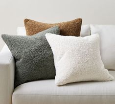 three pillows are sitting on the back of a white couch in front of a wall