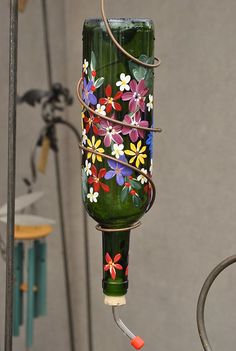 a green glass bird feeder with flowers painted on it's side and wire wrapped around the bottom