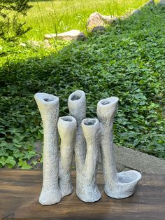 four cement vases sitting on top of a wooden table in front of some bushes