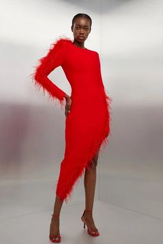 a woman in a red dress with feathers on the bottom and legs, standing against a white background