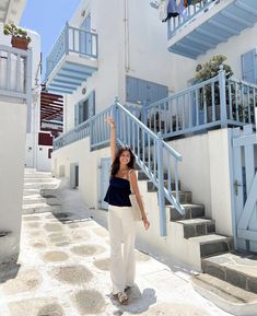 a woman standing in front of a white building with blue balconies and stairs