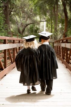 two people walking across a bridge wearing graduation gowns and holding onto each other's shoulders