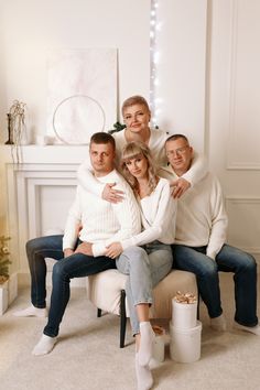 a family sitting on a chair in front of a fireplace posing for a christmas photo