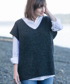 a woman is standing on the beach wearing a gray sweater and blue jeans with her hand in her hair