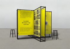 an exhibit with yellow panels and stools in front of the wall, on which there is a large poster