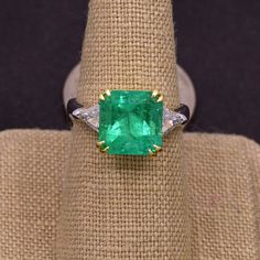 Absolutely stunning Colombian emerald mounted with 18k yellow gold  and platinum shank ! The 5.17CT emerald is from Colombia, beautiful rich green color and good clarity for its size. There are two sparkly trillion cut white diamonds adorning the center stone totaling 0.90 carat! This ring comes with one certification: Gemological Institute of America (GIA) Ring Size: 7 Total Weight: 8.2 grams Precious Metal: Platinum, 18k yellow gold Precious stones: -Emerald Center Stone: 5.17 carats, 10mmx10m Luxury Gia Certified Emerald Cut Gemstones, Luxury Gia Certified Emerald Gemstones, Luxury Emerald Gemstones With Prong Setting, Luxury Trillion Cut Emerald Ring For Formal Occasions, Luxury Trillion Cut Diamond Emerald Ring, Luxury Green Diamond Ring With Brilliant Cut, Luxury Trillion Cut Emerald Diamond Ring, Formal Gia Certified Emerald Gemstones, Fine Jewelry Emerald With Center Stone