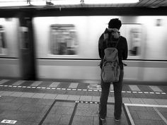 a person with a backpack standing in front of a train at a subway station as the train passes by