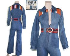 This deadstock 70s-era jumpsuit features a lovely vintage wash denim with western style serape patchwork and shoulder epaulettes on the bodice, matching belt with huge brass "militaires equipment" buckle, interesting 60s/70s style hip pockets, and flared bell bottom pant legs. This piece has never been worn and still has original price tag attached. Jumpsuit is 100% cotton, unlined and zips up the front. Best fits size xxs or xs (please check measurements below). Accessories not included. Payment plans available. Approximate Flat Measurements:  Multiply times 2 for bust, waist, and hip measurements. For best fit, compare with a similar style of clothing which you already own.  Total Length: 56.5" Bodice Length: 15.5" Pant Length: 41" Inseam: 31" Rise: 12" Shoulder to Shoulder: 14" Sleeve L Vintage Jumpsuits And Rompers For Fall, Retro Cotton Fitted Jumpsuits And Rompers, Fitted Blue Denim Retro Jumpsuit, Retro Fitted Long Sleeve Jumpsuits And Rompers, Vintage Cotton Fitted Denim Jumpsuit, Spring Vintage Fitted Denim Jumpsuit, Vintage Fitted Denim Jumpsuit For Summer, Blue Fitted Vintage Denim Jumpsuit, Vintage Fitted Long Sleeve Denim Jumpsuit