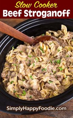 slow cooker beef stroganonoff in a black crock pot with a wooden spoon