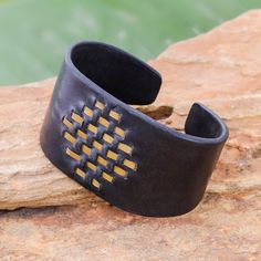 a black leather cuff with gold squares on the inside and outside, resting on a rock