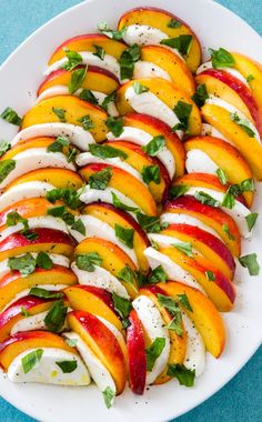 a white plate topped with sliced peaches and mozzarella cheese covered in mint