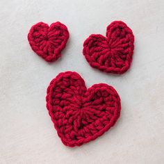 three red crocheted hearts sitting on top of a white surface