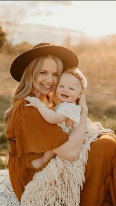 a woman holding a baby in her arms and smiling at the camera while wearing a hat